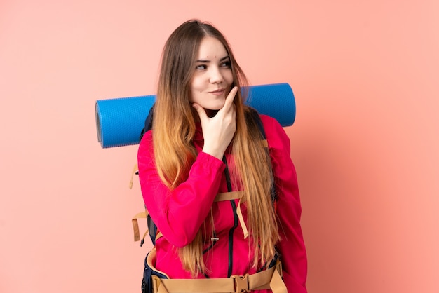 Ragazza giovane alpinista con un grande zaino isolato sulla parete rosa che pensa un'idea