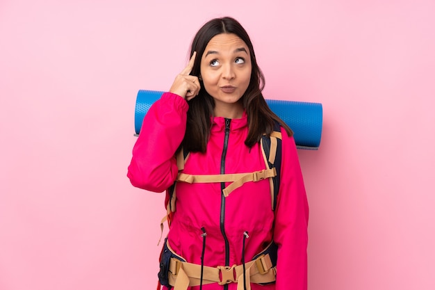 Ragazza giovane alpinista con un grande zaino sopra il colore rosa isolato che pensa un'idea