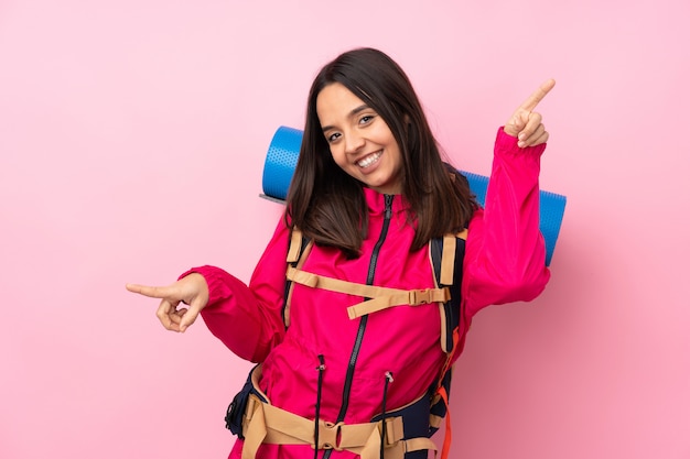 Ragazza giovane alpinista con un grande zaino sopra la parete rosa isolata che indica barretta ai laterali e felice