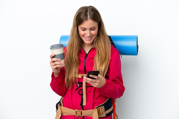 Ragazza giovane alpinista con un grande zaino su sfondo bianco isolato tenendo il caffè da portare via e un cellulare