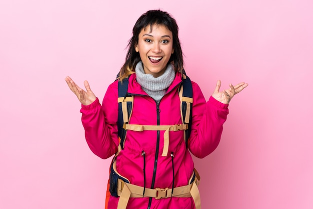 Ragazza giovane alpinista con un grande zaino sul muro rosa con espressione facciale a sorpresa