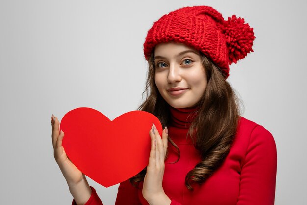 Ragazza giovane che mostra cuore rosso dal cartone alla fotocamera