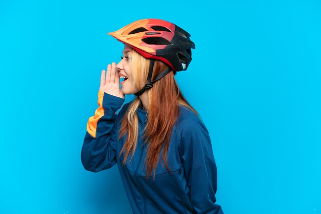 Ragazza giovane ciclista isolata su sfondo blu che grida con la bocca spalancata di lato