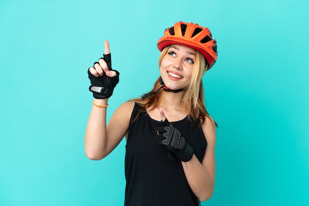 Ragazza giovane ciclista su sfondo blu isolato che indica con il dito indice una grande idea