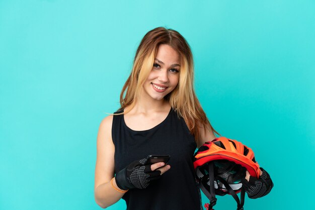 Ragazza giovane ciclista su sfondo blu isolato che invia un messaggio con il cellulare