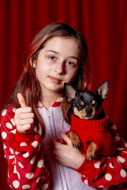 Ragazza giovane con cane. Adolescente in pigiama e un chihuahua vestito con un maglione rosso per cani