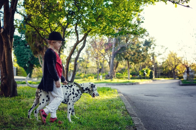 Ragazza giovane con i suoi cani dalmata in un parco di primavera. Ora del tramonto, rosso, bianco e nero