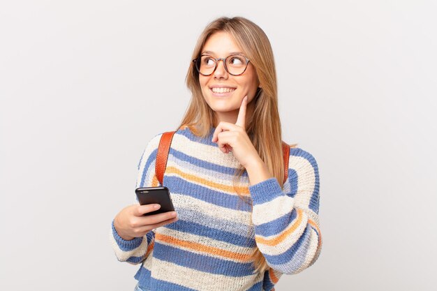 Ragazza giovane con una cella che sorride felice e sogna ad occhi aperti o dubita