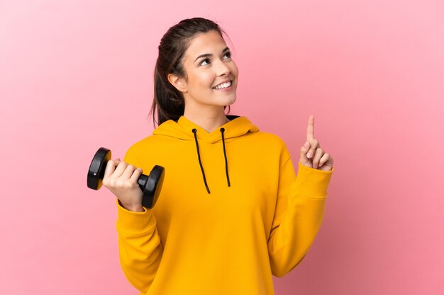 Ragazza giovane di sport che fa sollevamento pesi sopra fondo rosa isolato che indica una grande idea