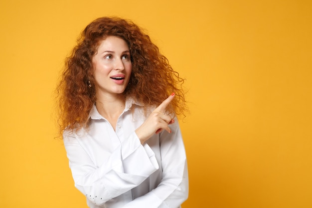 Ragazza giovane donna dai capelli rossi stupita in camicia bianca in posa isolata sul muro giallo arancione