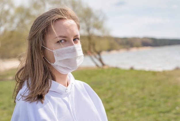 Ragazza, giovane donna nella mascherina medica sterile protettiva sul suo viso che guarda l'obbiettivo all'aperto si chiuda.