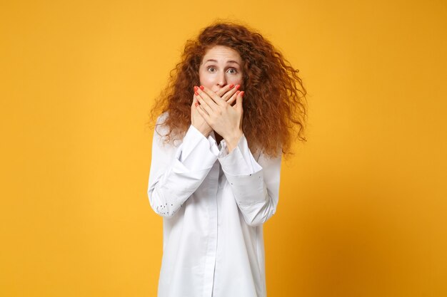 Ragazza giovane donna rossa scioccata in camicia bianca casual in posa isolata sul muro giallo arancione