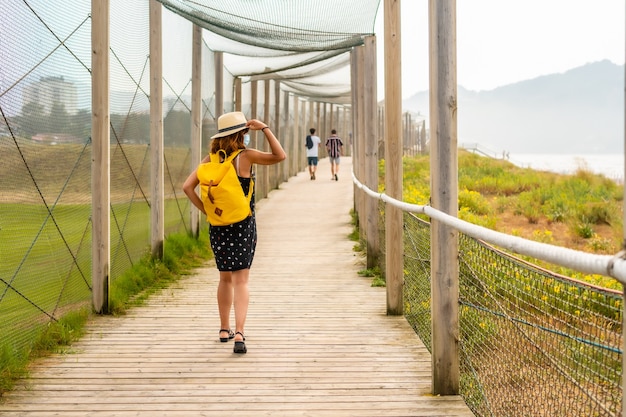 Ragazza giovane e avventurosa che si gode l'estate passeggiando da sola lungo la spiaggia con uno zaino giallo