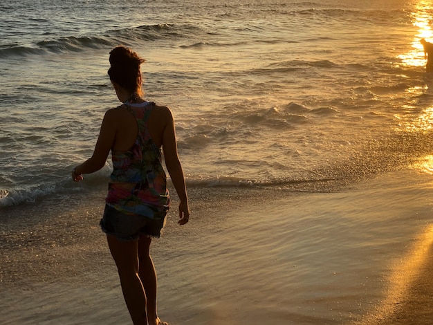 Ragazza giovane guardando il tramonto sulla spiaggia di Barra da Tijuca a Rio de Janeiro, Brasile. Mare con onde calme.