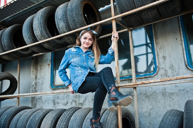 Ragazza giovane hipster in giacca di jeans e sciarpa per la testa nella zona di montaggio dei pneumatici