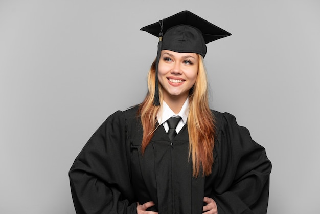 Ragazza giovane laureato universitario su sfondo isolato in posa con le braccia all'anca e sorridente