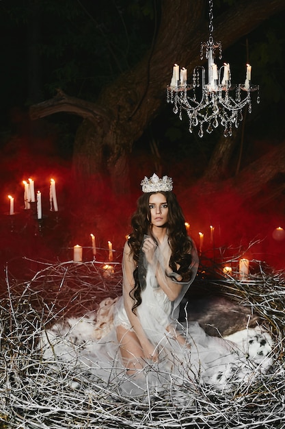 Ragazza giovane modella in lingerie di raso in posa in un enorme nido con fumo rosso e candele sullo sfondo