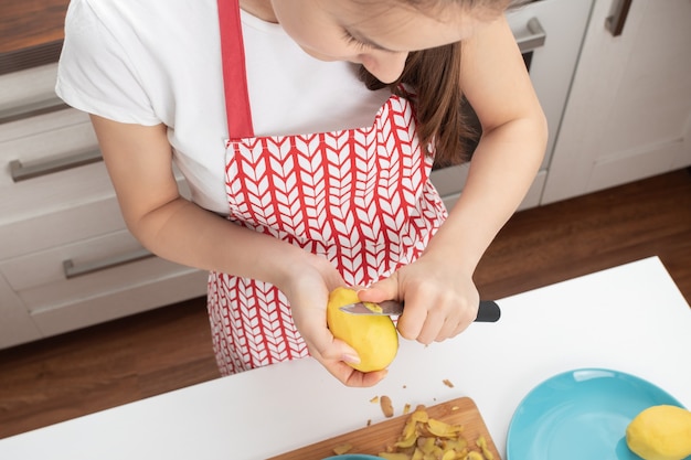 Ragazza giovane sbucciare le patate in cucina