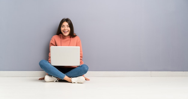 Ragazza giovane studente con un computer portatile sul pavimento con espressione facciale a sorpresa