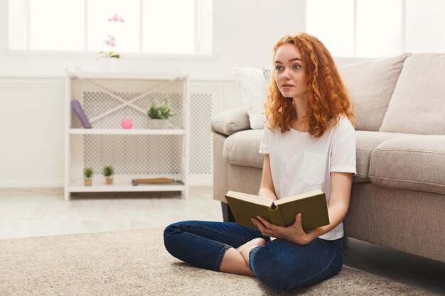 Ragazza giovane studentessa rossa che legge un libro. Ragazza che studia a casa sul pavimento