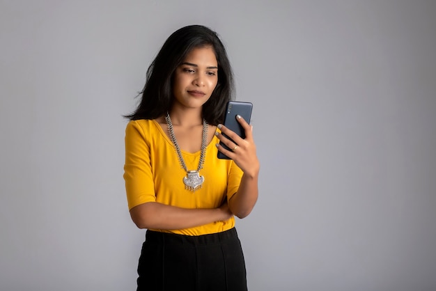 Ragazza giovane utilizzando il telefono cellulare o smartphone sul muro grigio