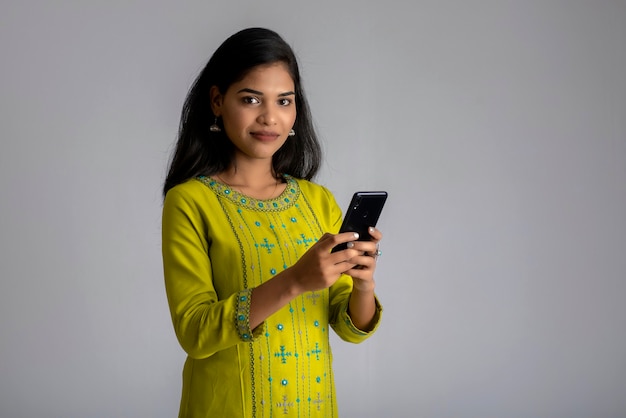 Ragazza giovane utilizzando il telefono cellulare o smartphone sul muro grigio