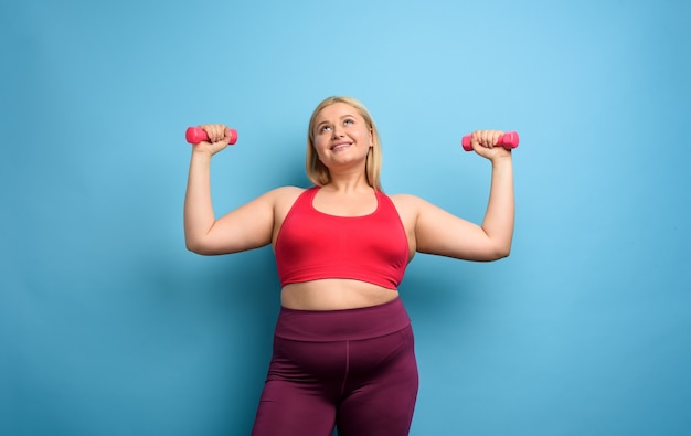 Ragazza grassa fa palestra a casa. espressione soddisfatta. Sfondo ciano