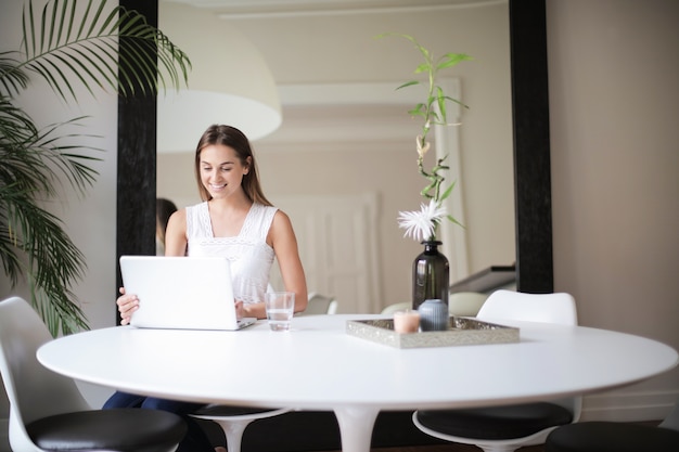 Ragazza graziosa a casa che lavora ad un computer portatile