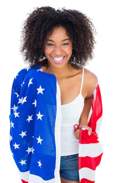 Ragazza graziosa avvolta nella bandiera americana che sorride alla macchina fotografica