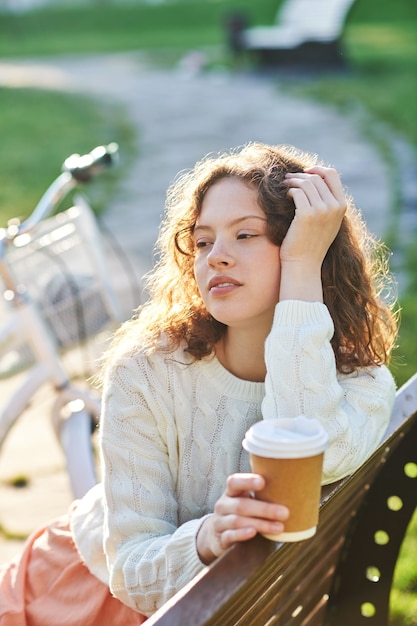 Ragazza graziosa che prende il caffè nel parco al mattino