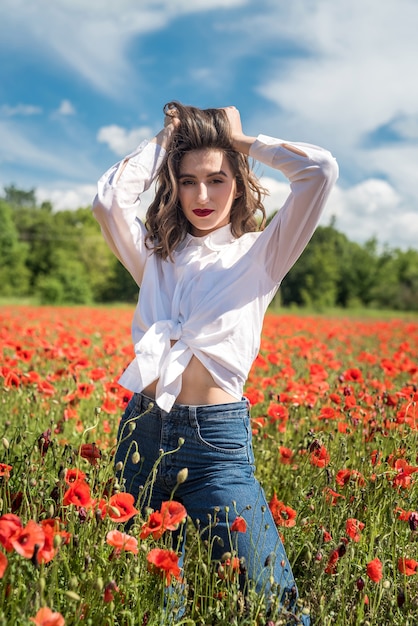 Ragazza graziosa che sogna e gode della natura al campo dei papaveri rossi. estate