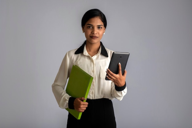 Ragazza graziosa che tiene il libro e utilizzando il cellulare su grigio