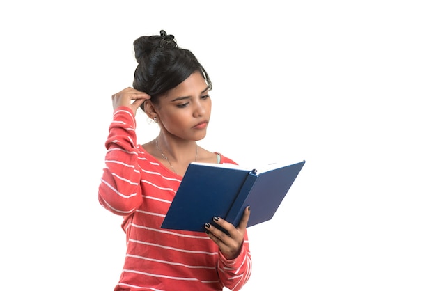 Ragazza graziosa che tiene libro e posa su sfondo bianco