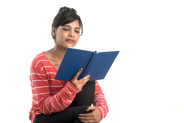 Ragazza graziosa che tiene libro e posa sul muro bianco