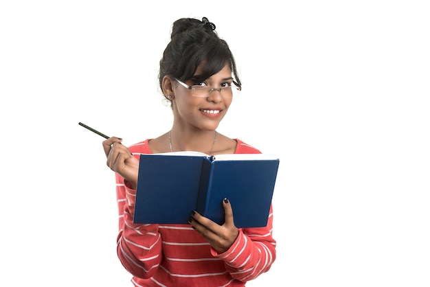 Ragazza graziosa che tiene libro e posa sul muro bianco