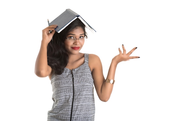 Ragazza graziosa che tiene libro e posa sul muro bianco