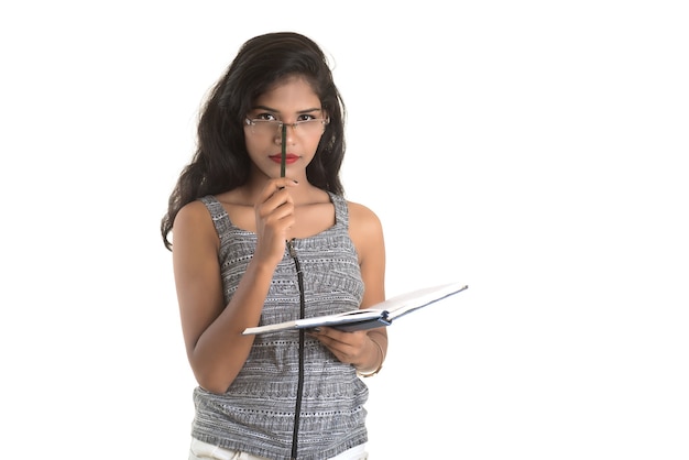 Ragazza graziosa che tiene libro e posa sul muro bianco