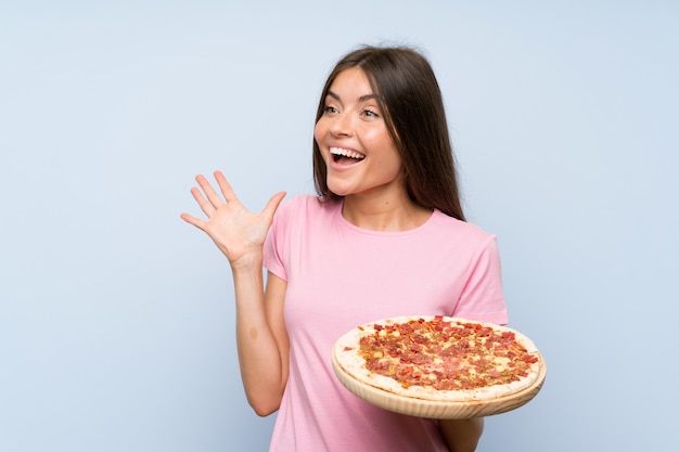 Ragazza graziosa che tiene una pizza con espressione facciale di sorpresa