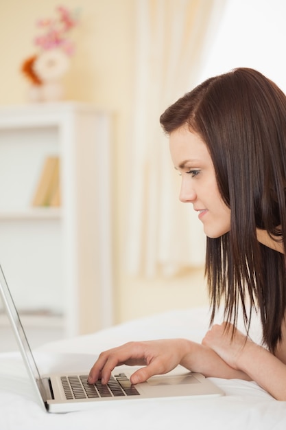 Ragazza graziosa che utilizza un computer portatile che si trova sulla sua base