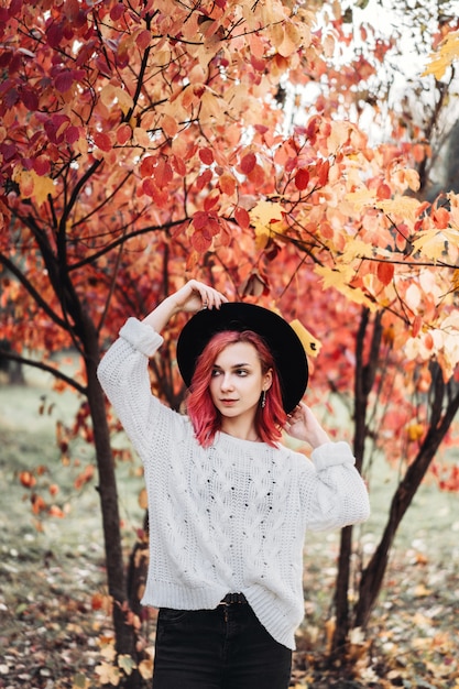 Ragazza graziosa con capelli rossi e cappello che camminano nel parco, tempo di autunno.