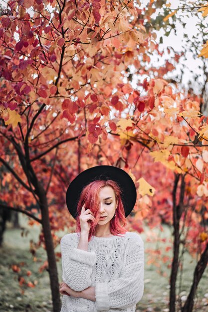 Ragazza graziosa con capelli rossi e cappello che camminano nel parco, tempo di autunno.