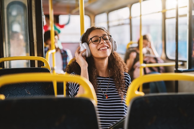 Ragazza graziosa con le cuffie che si siedono in un bus e che guardano compressa.