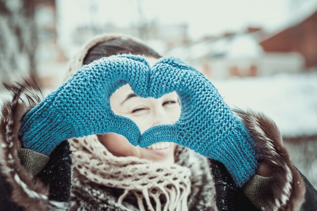 Ragazza graziosa con le mani a forma di cuore nei guanti