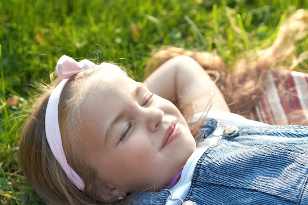 Ragazza graziosa del bambino che stabilisce sull'erba verde in estate schiacciando un pisolino.