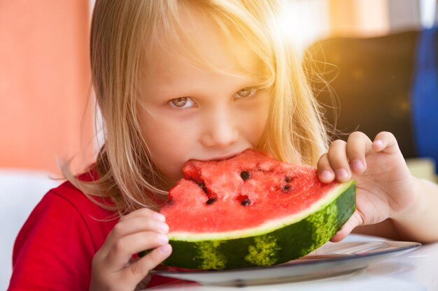 Ragazza graziosa del bambino di 4 anni che mangia il primo piano dell'anguria a casa che guarda l'obbiettivo