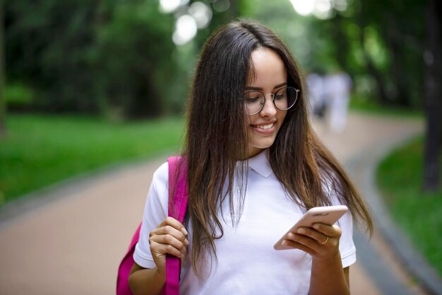 Ragazza graziosa dell'allievo che controlla gli orari delle classi tramite il telefono cellulare