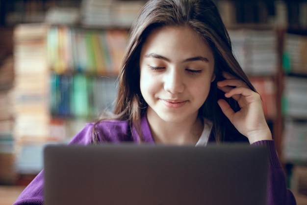 Ragazza graziosa della scuola che studia nella biblioteca della scuola usando il computer portatile