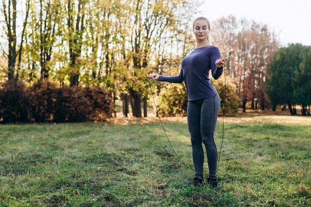 Ragazza graziosa e esile che salta sulla corda di salto all'aperto