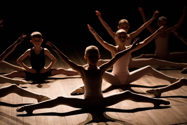 Ragazza graziosa e ragazzo seduto sul palco con stretching e formazione per i balli di balletto.