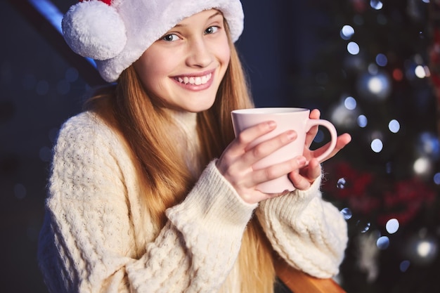 Ragazza graziosa sorridente che celebra il Natale con la cioccolata calda